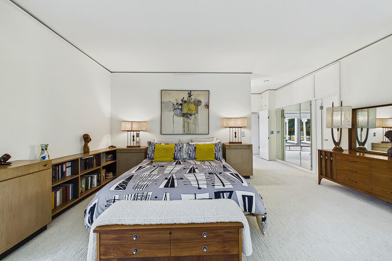 A bedroom with glass on two sides looking into trees.
