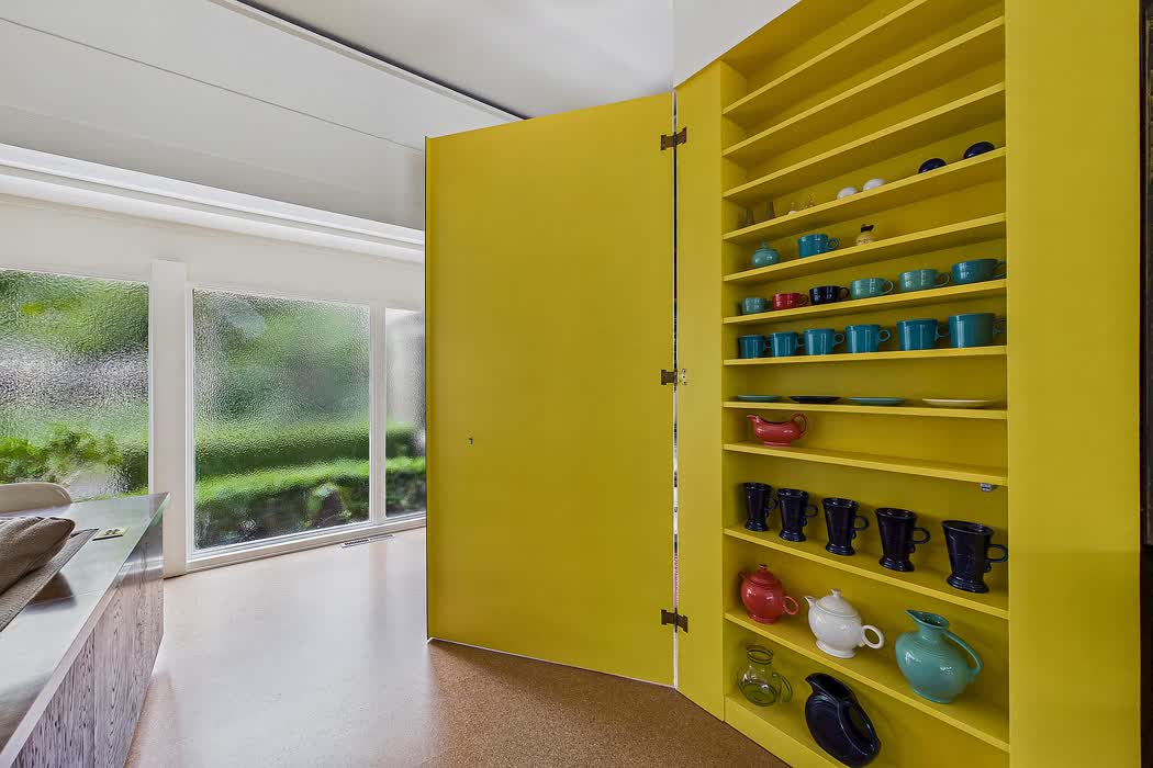 A tall built-in pantry lacquered bright yellow, filled with coloured glass.
