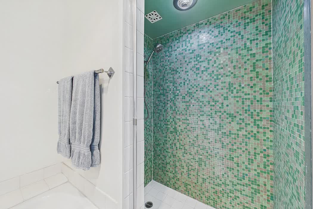 A shower lined floor to ceiling in small green glass mosaic.