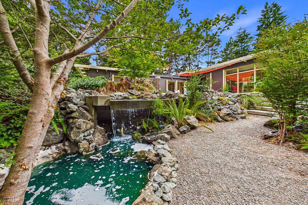 The jade koi pond seen along its length, with a rock waterfall and the house beyond.